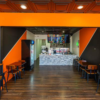 Interior with orange accents and dark walls, table seating and a counter area.