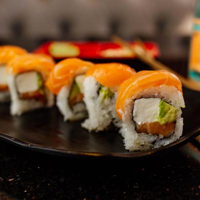 Sushi rolls topped with salmon on a black plate.