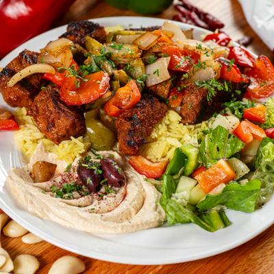 Mediterranean platter with beef kebabs, yellow rice, fresh salad, and hummus.