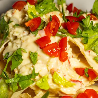 White chicken nachos topped with melted cheese, red diced tomatoes, and fresh green lettuce.