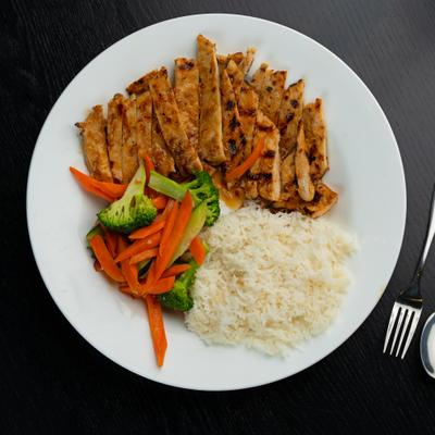 Grilled chicken served with rice, carrots, and broccoli on a white plate.