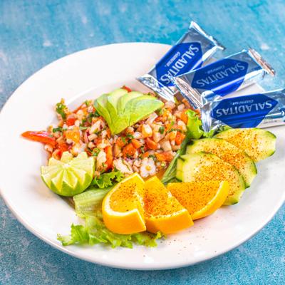 Shrimp ceviche with avocado, cucumbers, oranges, lime, and packaged crackers.