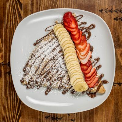 Crepe topped with sliced strawberries and bananas, chocolate sauce and powdered sugar.