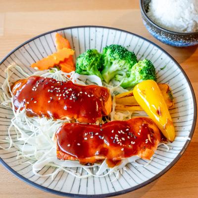 Salmon Teriyaki served over a bed of shredded cabbage, with vegetables on the side.