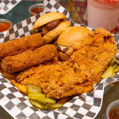 A platter with beef sliders, mozzarella sticks, chicken tenders, fries, pickles, and sauce dips.