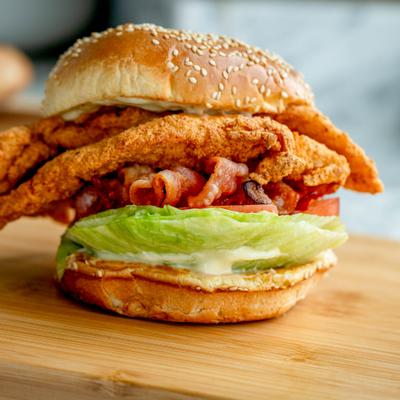 Crispy chicken BLT sandwich served on a wooden board.