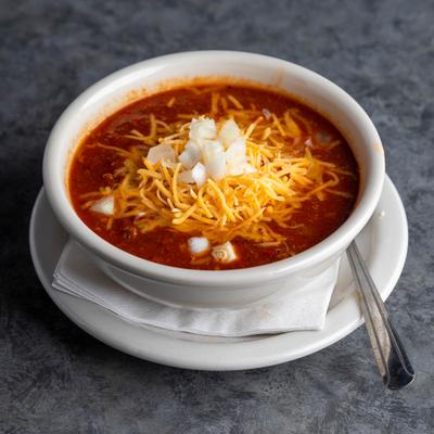 A bowl of chili topped with shredded cheddar cheese and diced raw onion.