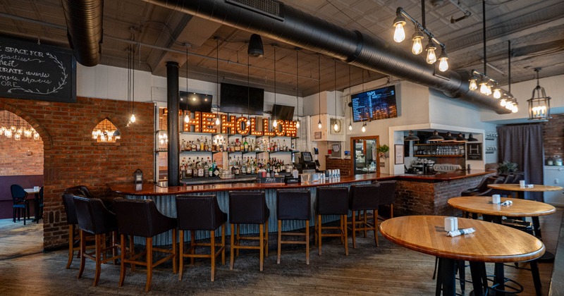 Interior of a bar with a curved bar counter, leather stools, and exposed brick walls