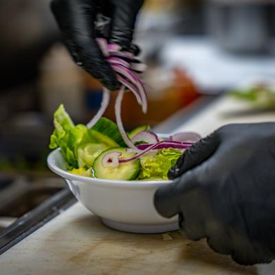 An employee placing salad ingredients into a bowl at salad bar.