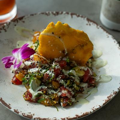 A colorful poke dish with tuna, vegetables, cream sauce, and a fried plantain.