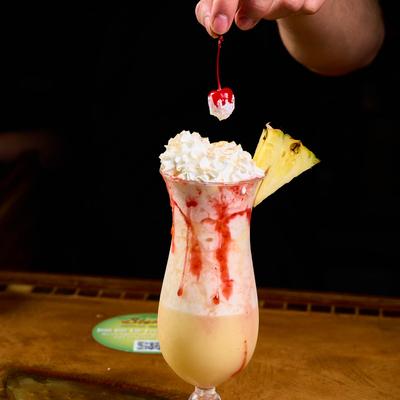 A hand garnishing a tropical cocktail with a cherry.