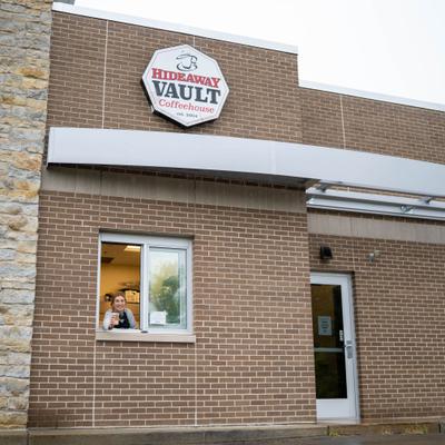 The exterior of the HideAway Vault Coffeehouse with an employee at a drive-thru window.