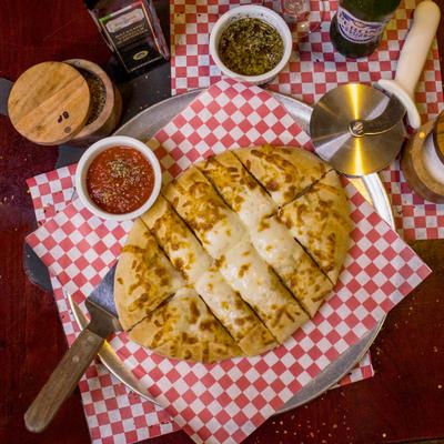 Cheese bread surrounded by marinara sauce, drinks, and spices.