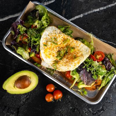 Avocado toast topped with mixed greens, cherry tomatoes and fried egg.