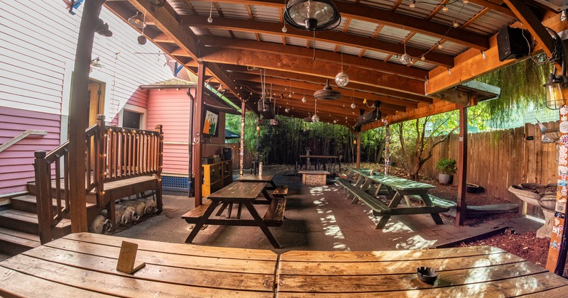 Covered patio area featuring wooden picnic tables, string lights, and greenery
