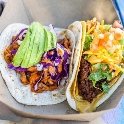 Two distinct tacos with various toppings served in a carboard box.