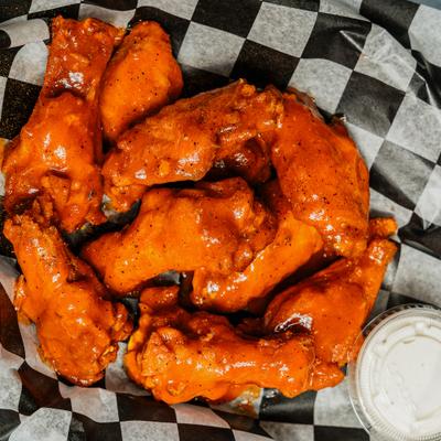 Buffalo-style chicken wings served in a basket with a side of dipping sauce.