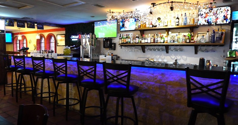 A bar with high-backed chairs, blue lighting and shelves of liquor bottles, with TVs