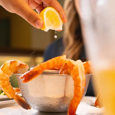 A hand squeezing lemon over a bowl of shrimp.