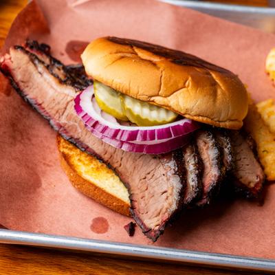 A sliced brisket sandwich topped with red onions and pickles beside crinkle-cut fries.