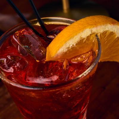 Red cocktail garnished with an orange slice.