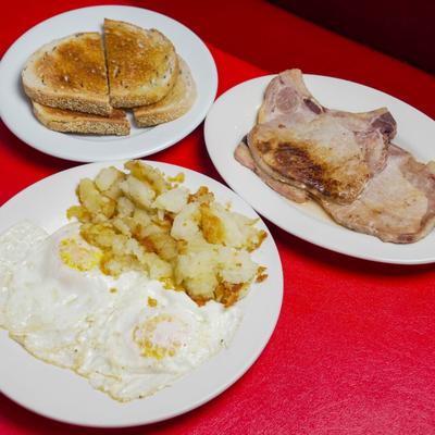 Fried eggs with home fries served alongside pork chips and toasted bread.