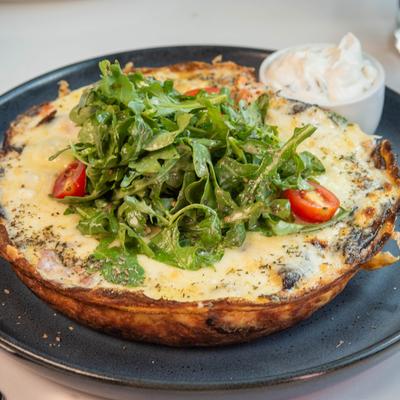 A golden, cheesy frittata on a black plate topped with fresh arugula.