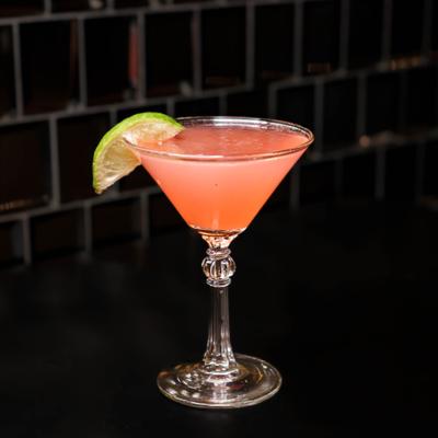 Pink cocktail in a martini glass with lime garnish.