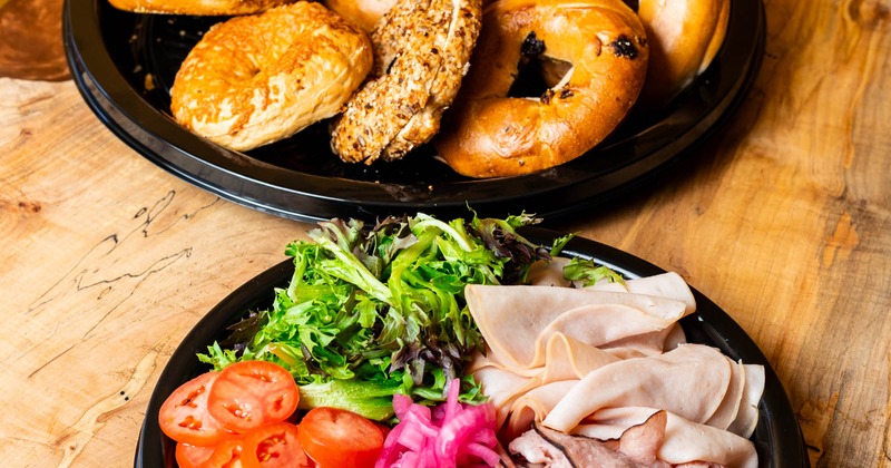 A plate with assorted bagels and a plate with cured meats and vegetables