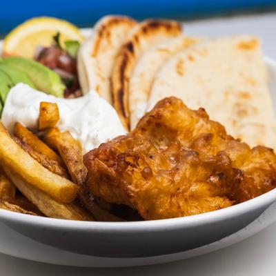 Fried fish with fries, tzatziki, avocado, salad, and pita bread, close up.