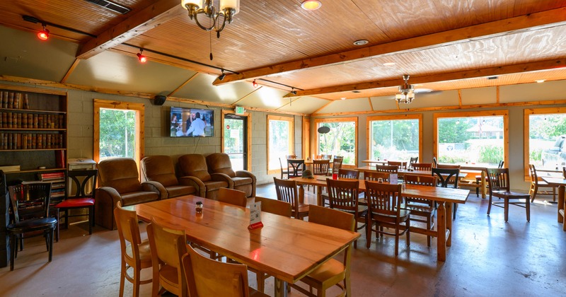 A cozy dining area - wooden tables and chairs, a leather sofa, a bookshelf, a flat-screen TV