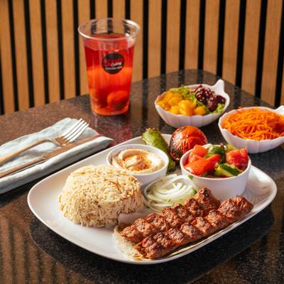Beef kebab skewers, with rice, hummus, salad, and a cocktail drink.
