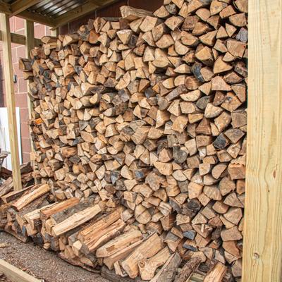 Neatly stacked pile of split firewood housed in an outdoor storage shed.