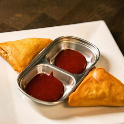 Sambusa pastry filled with ground beef, served with a red sauce for dipping.