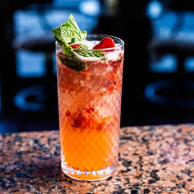 Orange cocktail in a textured highball glass, with mint and strawberry garnish.