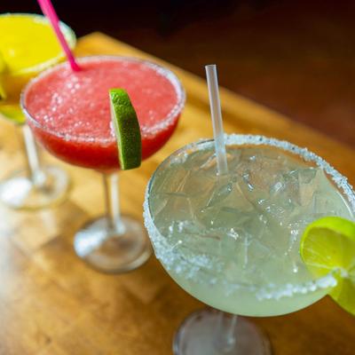 Three colorful margaritas on a wooden table, each with a lime wedge.