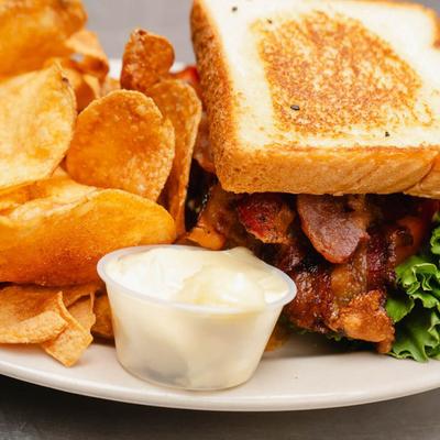 BLT sandwich served with sides of chips and a dipping sauce, close-up.