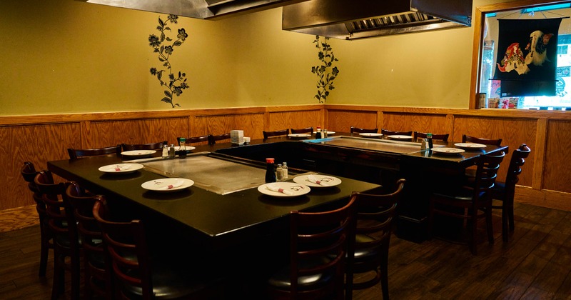 Empty hibachi restaurant dining area with wood paneled walls, black cooking tables