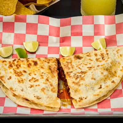 Two quesadilla halves sit on checkered paper with lime wedges.