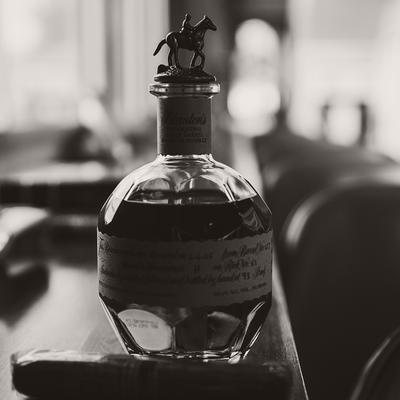A bottle of bourbon and a cigar rest on a bar counter.
