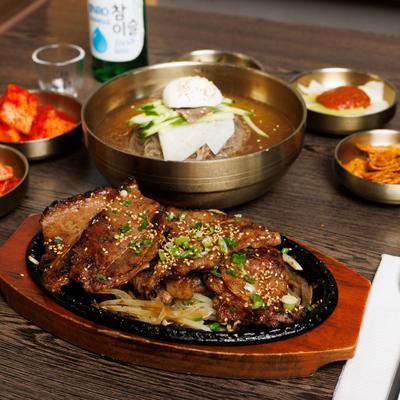 Korean BBQ short ribs served beside cold buckwheat noodles and various sides.