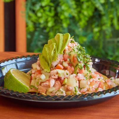 Seafood salad topped with avocado and cilantro on a plate with a lime wedge.