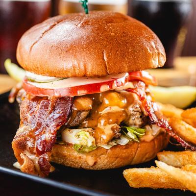 Bacon cheeseburger with lettuce, tomato, melted cheese, and sauce, served with fries.