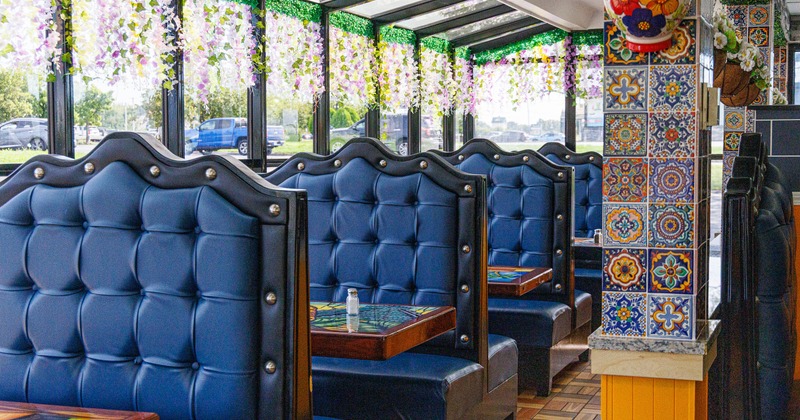 Colorfully decorated restaurant interior with blue booths, hanging flowers, patterned tables, and a tiled column