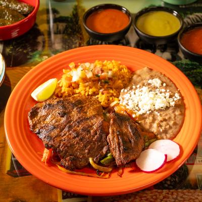 Carne asada plate with rice, refried beans, radishes, and salsas.