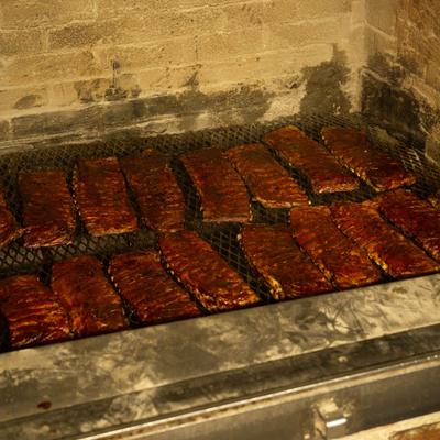 Racks of glazed barbecue ribs being slow-cooked in a hickory-wood pit.