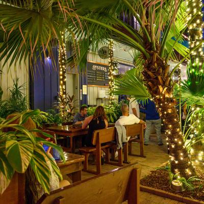 Diners sit at tables under palm trees strung with warm fairy lights.