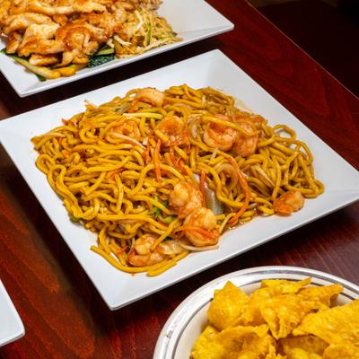 Shrimp Lo Mein in focus among multiple food dishes.