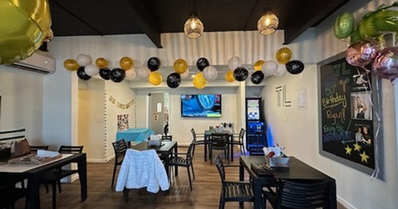 Decorated venue space for a birthday celebration with tables, chairs and baloons