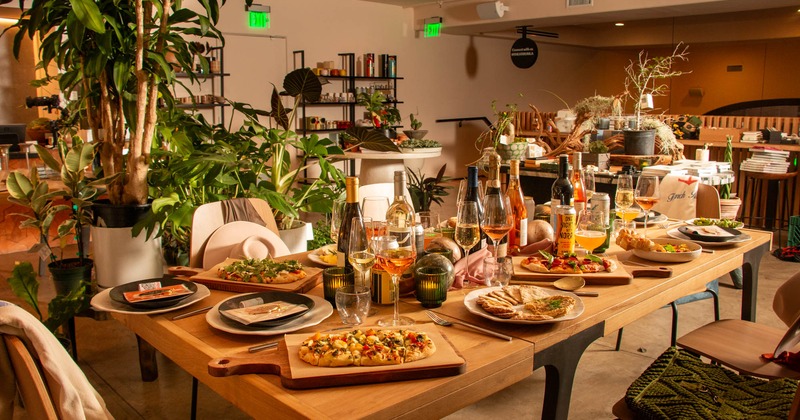 Interior, a long wooden table laden with various dishes and multiple bottles of wine and glasses